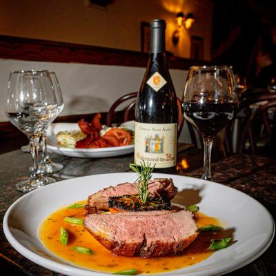 Roasted meat dish served with sauce beside a wine bottle.