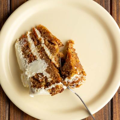 A white plate holds a slice of carrot cake on a wooden table.