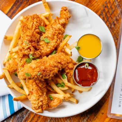 Fried chicken tenders with fries, ketchup, and honey mustard, top view.