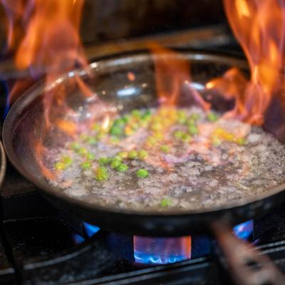 Flaming pan with sauce and green peas cooking on a gas stove.