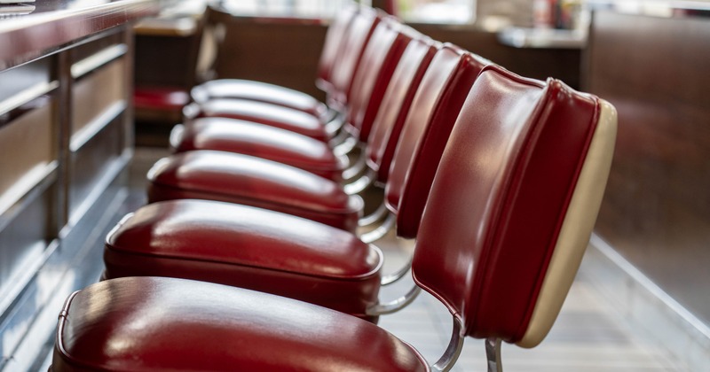 Row of empty red leather bar stools with chrome bases