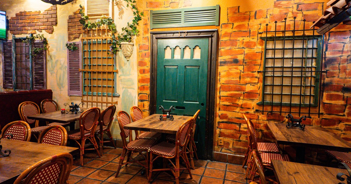 A restaurant interior with faux brick walls, and wicker chairs around wooden tables