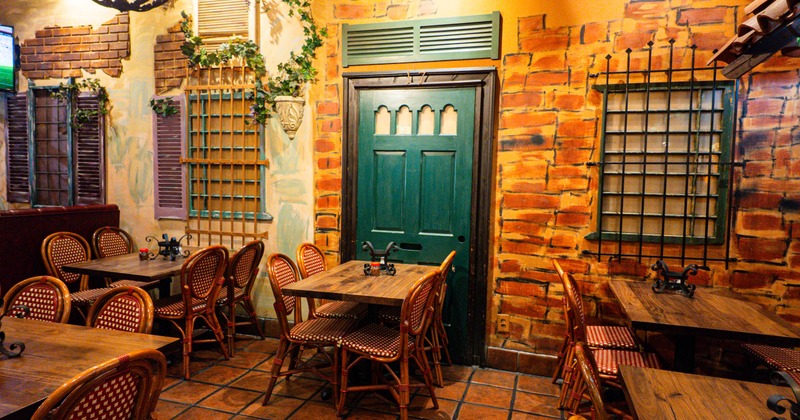 A restaurant interior with faux brick walls, and wicker chairs around wooden tables