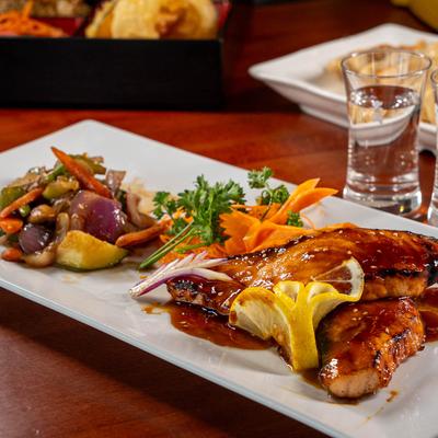 Salmon teriyaki plate set next to shots of drink.