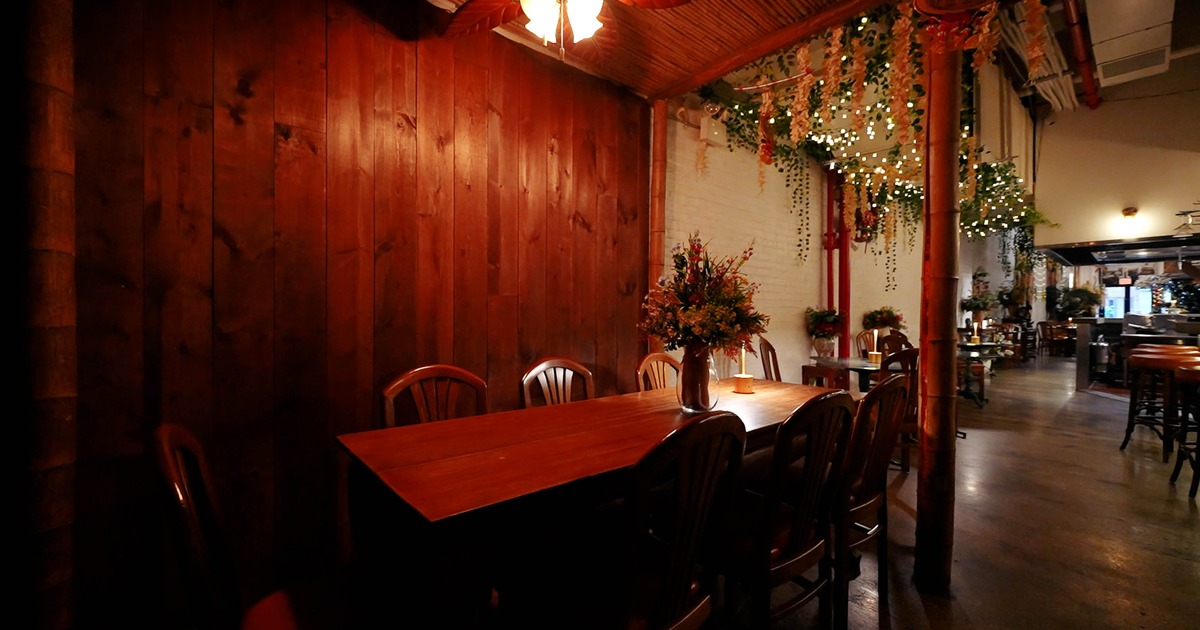 A cozy dining area with a long wooden table, chairs, hanging greenery and warm lighting.