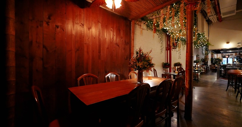 A cozy dining area with a long wooden table, chairs, hanging greenery and warm lighting.