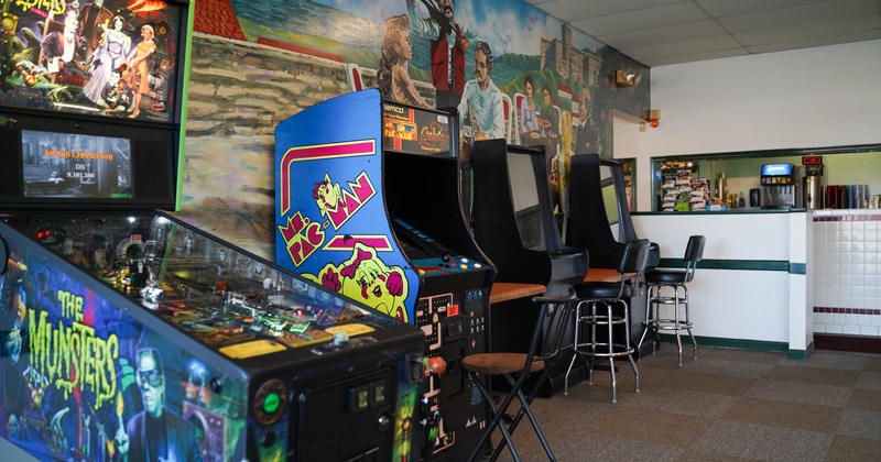 Vintage arcade machines with stools against a colorful mural