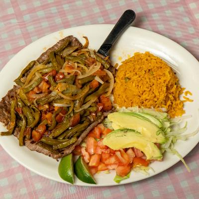 Carne asada plate with rice, lettuce salad avocado, pico de gallo, and lime wedges.