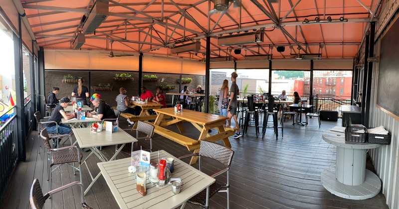 Terrace covered with awning, guests sitting at tables, staff in action