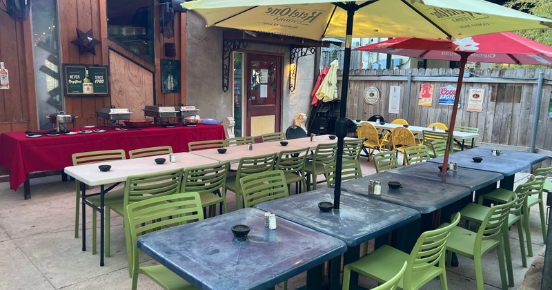 Outdoor patio seating area, a buffet with chafing dishes on a red tablecloth is set up nearby