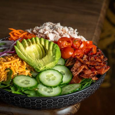 A salad bowl with avocado, cucumber, tomato, bacon, and other ingredients.