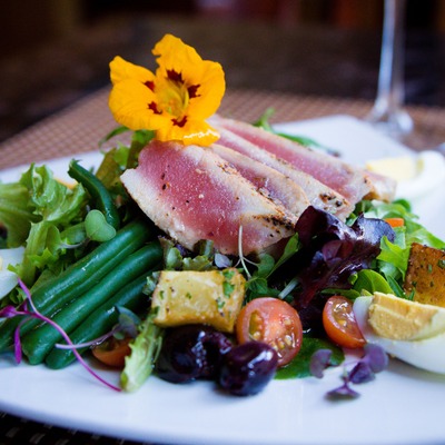 Seared tuna salad with mixed greens, eggs, tomatoes, and an edible flower.