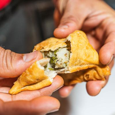 Hands pulling apart a vegetable samosa.
