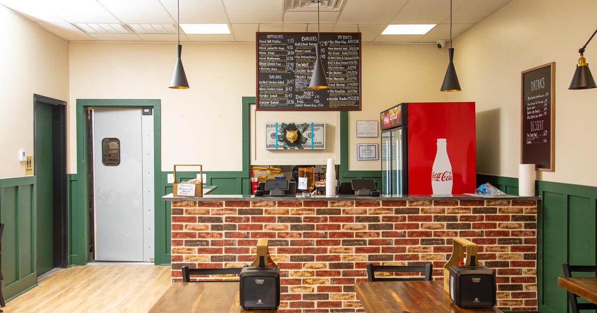 Interior of a small eatery with brick counter, pendant lights and menu boards.