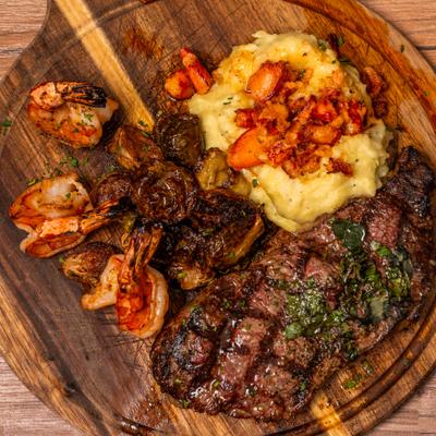 Surf and turf dish with grilled steak and shrimp on a rustic wooden serving board.