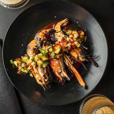Grilled prawns with pineapple salsa and sauce on a black plate.