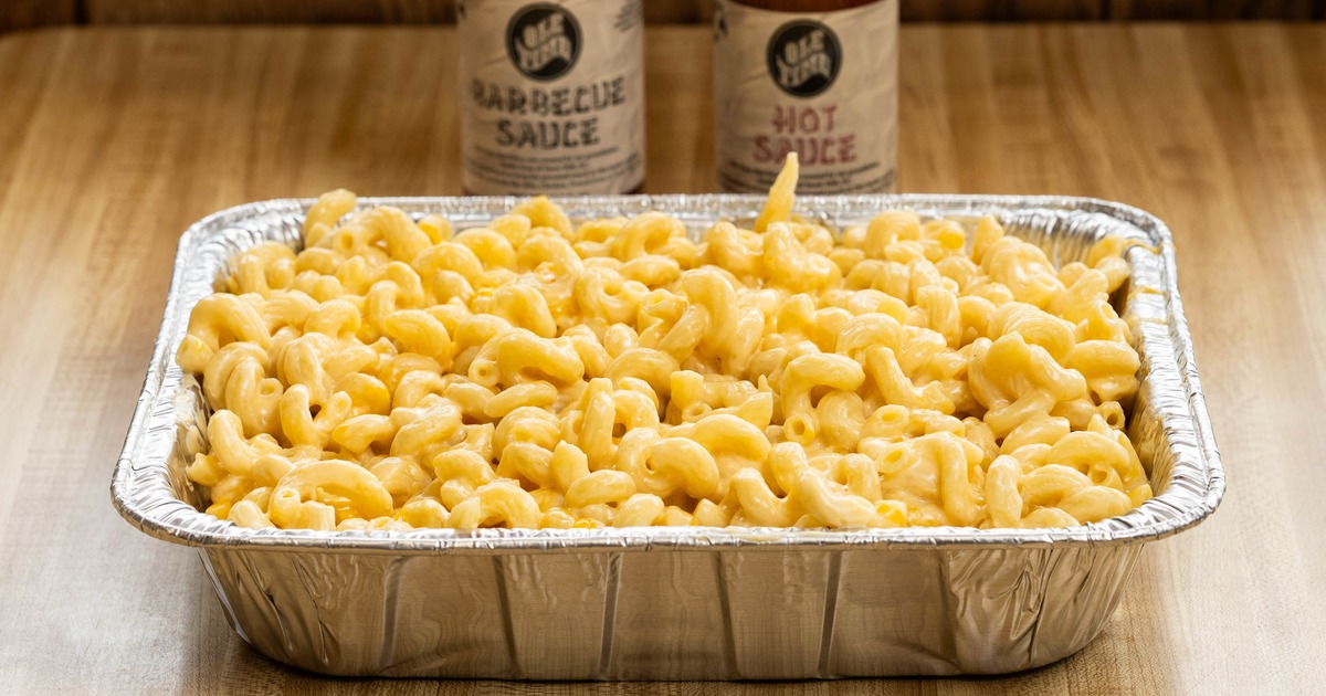 Mac and Cheese served in a catering tray alongside two bottles of sauces