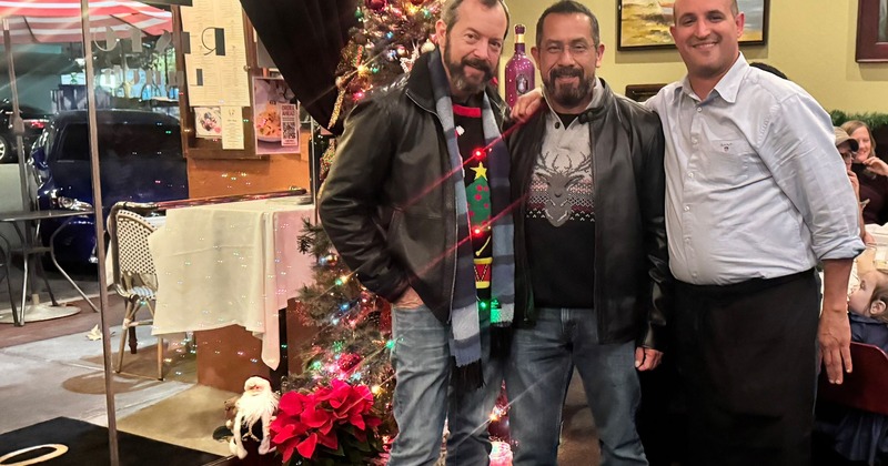 A group of people posing for a picture next to a Christmas tree inside a dining area