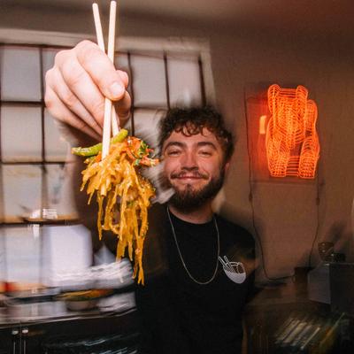 Person holding noodles with chopsticks in a kitchen.
