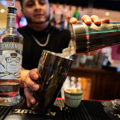 Bartender pours liquid from a shaker next to a bottle of vanilla vodka.
