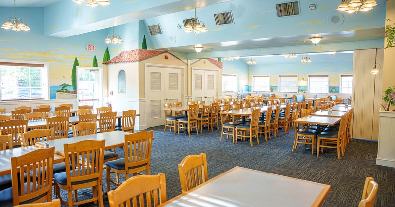 Bright and spacious dining room with wooden tables, chairs, and murals