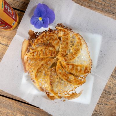 Pan-fried potstickers garnished with a flower and served with drink in a can.