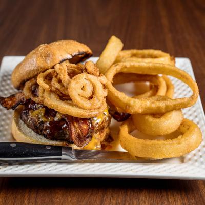 Bacon cheeseburger with melted cheese and crispy onion rings served with a side of onion rings.