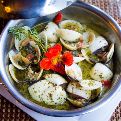 Steamed clams in herb broth garnished with an orange flower.