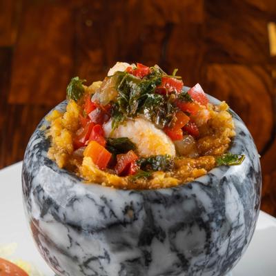 Shrimp with plantains, peppers, and collard greens in a ceramic bowl.
