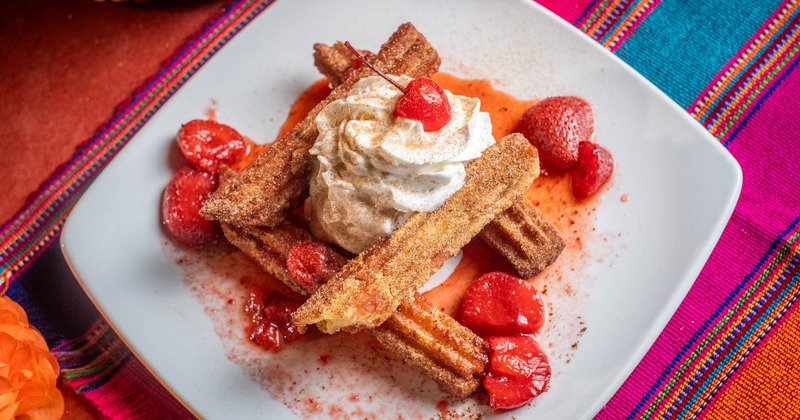 Churros with whipped cream, strawberries, and a cherry on a white plate