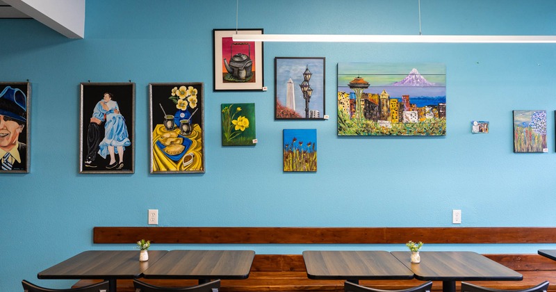 Interior, banquette bench with tables and chairs, various framed paintings on a blue wall