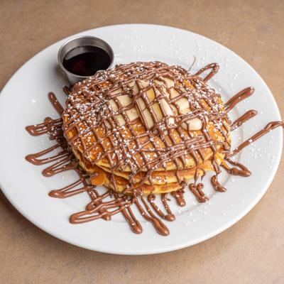 Pancakes topped with chocolate drizzle and powdered sugar, served with syrup.