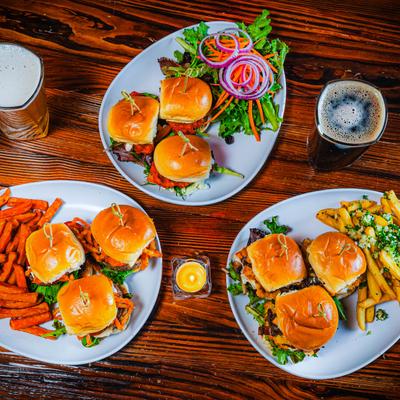 Three plates with sliders, fries, and salad on a table, accompanied draft beers.