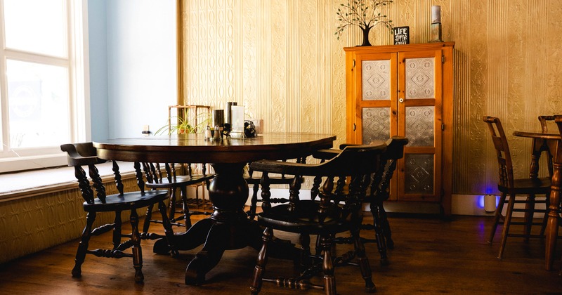 Interior, dining area featuring a large wooden round table surrounded by various wooden chairs