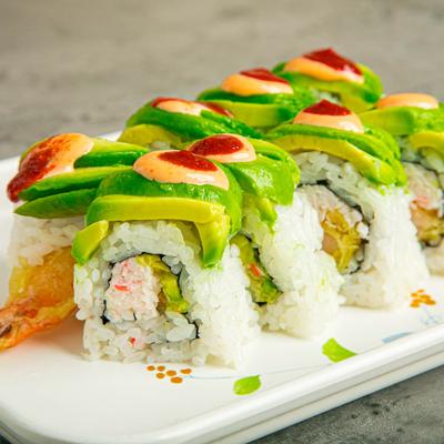 Sushi rolls topped with avocado and spicy mayo on a plate.