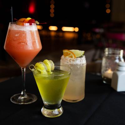 Three cocktails on a table, featuring vibrant colors and fresh garnishes.