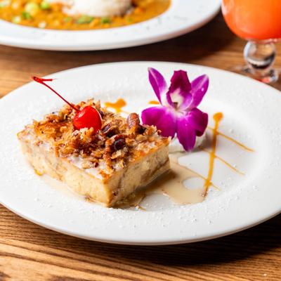 Bread pudding slice topped with pecans, caramel sauce, and a maraschino cherry.