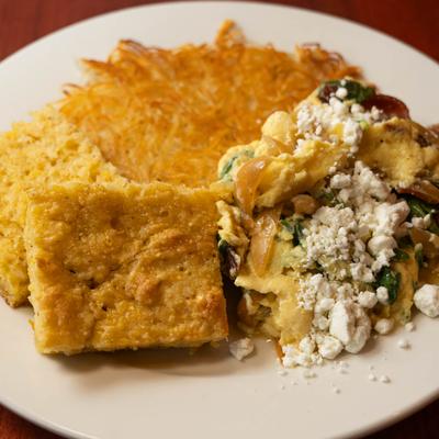 Scrambled eggs with bacon, arugula, onions, goat cheese, hash browns, and biscuits.