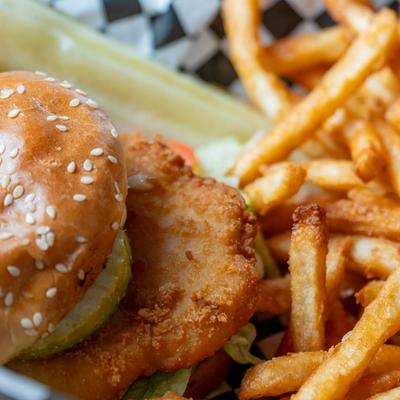 Close up of Fried chicken sandwich on a sesame bun, served with fries.