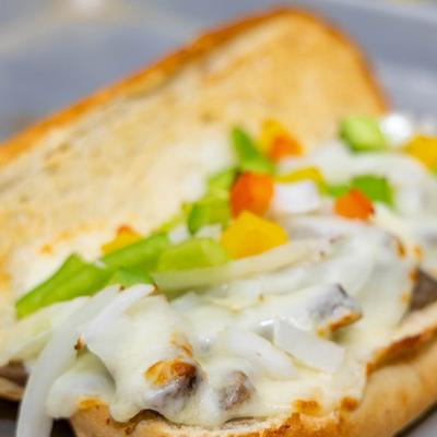 Close-up of a sandwich with melted cheese, colorful bell peppers, and onions on a toasted bun.