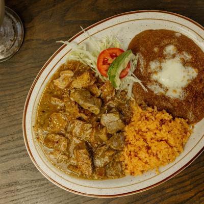 Chile verde accompanied by refried beans, rice, and a side salad.