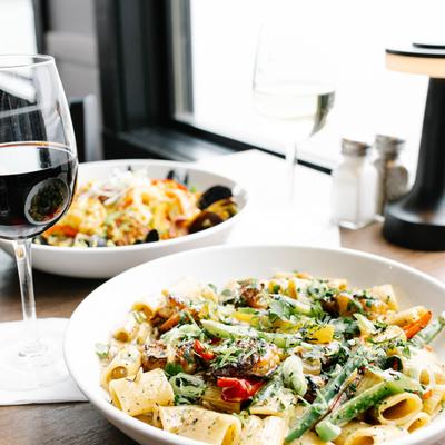 Jamaican Jerk Shrimp Rasta Pasta on a table by a window, with red wine and seafood paella.