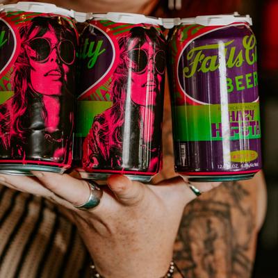 Hand holding a six-pack of vibrantly designed beer cans featuring a woman's portrait.