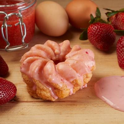 Strawberry cruller on a wooden board with fresh eggs and strawberries nearby.