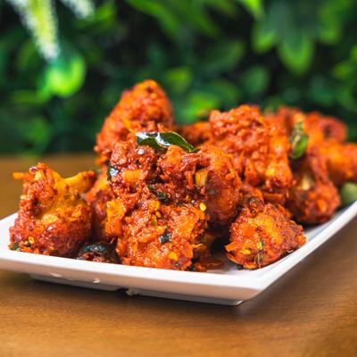 Spicy fried chicken pieces topped with curry leaves on a white plate.