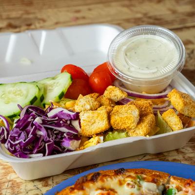 To-go salad with cucumbers, croutons, cherry tomatoes, and a side of ranch.
