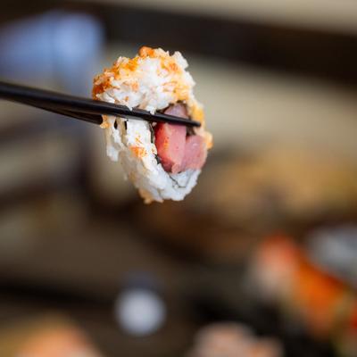 A piece of sushi being held with chopsticks, close up.