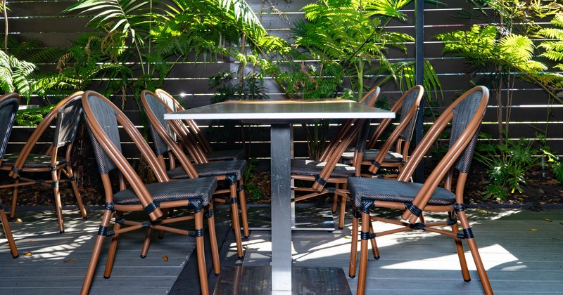 Outdoor patio table and folding chairs surrounded by lush ferns and palm plants