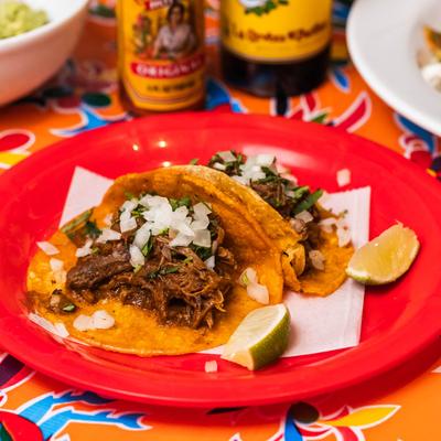 Carnitas Tacos with shredded meat, onions, and cilantro on a red plate.
