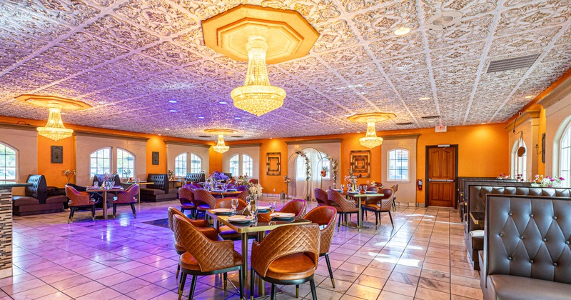 Interior, dining room with crystal chandeliers, orange walls, set tables, and purple lighting